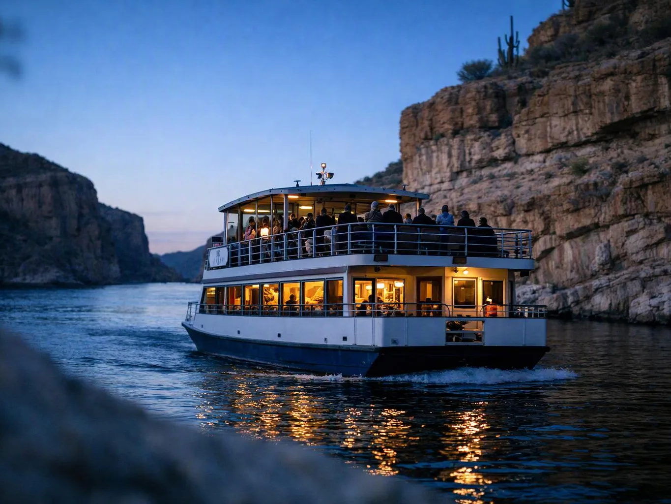 A lit riverboat carries passengers between steep canyon cliffs at dusk